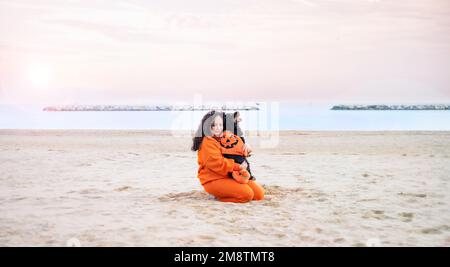 Halloween cane vestito come una zucca sulla spiaggia. Black Cocker Spaniel in abiti festosi gioca con il suo proprietario. Autunno terrapieno e una bella passeggiata. Sentimenti teneri con gli animali domestici Foto Stock