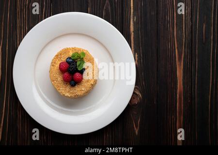 Torta di Napoleone con bacche e menta, su un piatto, su un fondo di legno Foto Stock