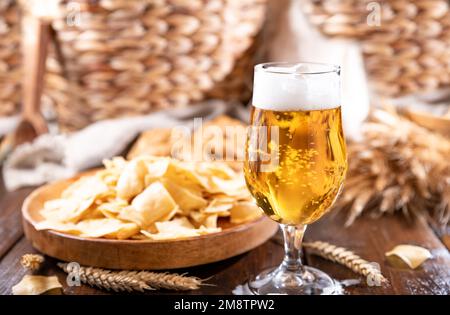Bicchiere di birra artigianale leggera su un tavolo di legno. La birra viene versata in un bicchiere con schiuma e bolle. per i social media. consistenza della birra. Su un piatto ci sono patatine tradizionali in Italia in Sardegna Foto Stock