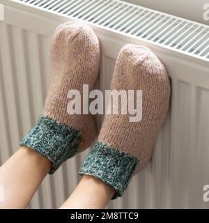 Una donna riscalda i piedi in calzini di lana su un radiatore. Riscaldamento domestico. Bassa temperatura e freddo in casa. Primo piano della foto Foto Stock