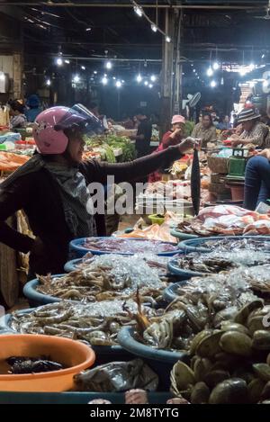 Acquisto di pesci indossando un casco rosa: Phsar Chas (Old Market), Siem Reap, Cambogia Foto Stock