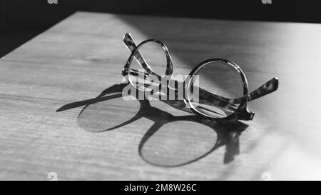 Bicchieri su tavolo di legno. Sole che si riflette sugli occhiali vintage sul tavolo. Concetto di saggezza. Copia spazio per il testo. Backgroun bianco e nero Foto Stock