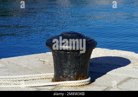 Un palo di metallo nero per l'ormeggio delle navi avvolto in una corda bianca spessa in un porto marittimo Foto Stock