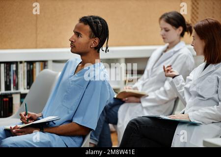 Ritratto degli studenti di medicinali seduti in fila nel pubblico durante una lezione o un seminario, focalizzato sul giovane nero in primo piano Foto Stock