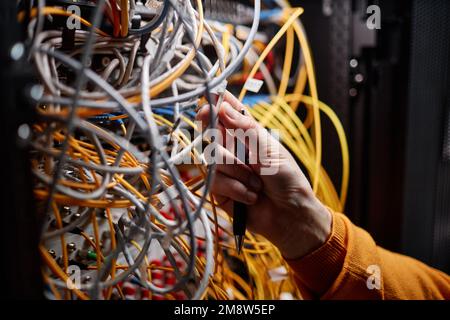 Primo piano del tecnico che collega i cavi e i fili nell'armadietto del server durante la configurazione della rete Internet, spazio di copia Foto Stock