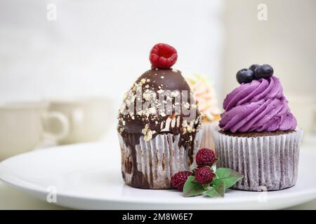 Tortine colorate con crema frostinata e frutti di bosco. Cupcake al mirtillo e al cioccolato. Dessert decorato. Foto Stock