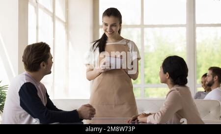 Cameriera giovane e graziosa, con grembiule uniforme, che serve coppie diverse Foto Stock