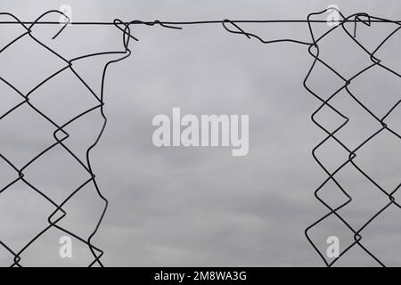 Il foro della recinzione della maglia della catena danneggia le forme dei fili e lo sfondo del cielo nuvoloso. Foto Stock