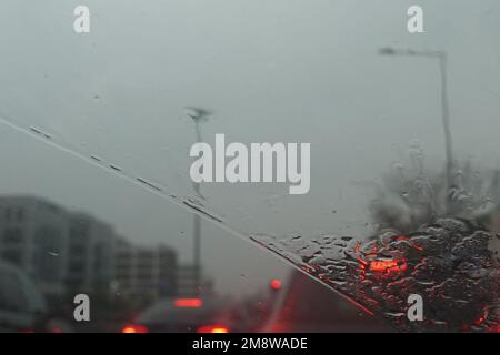 Traffico attraverso il parabrezza dell'auto in una giornata piovosa. Sfocatura astratta. Foto Stock