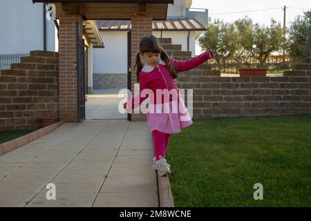 Immagine di una adorabile bambina che torna dalla scuola giocando a piedi su un marciapiede mentre si bilancia. Foto Stock