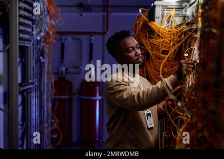 Vista laterale ritratto di giovane uomo nero come amministratore di sistema che lavora con server in luce al neon, spazio copia Foto Stock