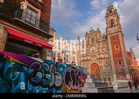 Un muro graffito che porta alla facciata churrigueresque della Parroquia de la Santísima Trinidad nel quartiere zona Centro di Città del Messico, Messico. Foto Stock