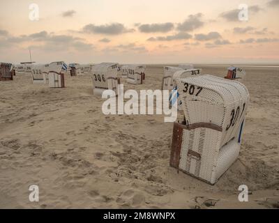 Sedie a sdraio numerate sulla sabbia di un'isola sotto il cielo nuvoloso al tramonto nella città di Spiekeroog Foto Stock