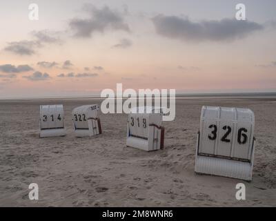 Sedie a sdraio numerate sulla sabbia di un'isola sotto il cielo nuvoloso al tramonto nella città di Spiekeroog Foto Stock