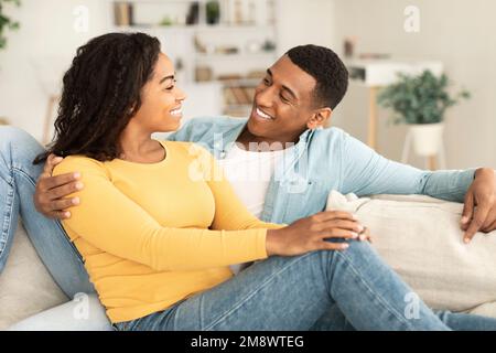 Felice giovane afroamericano maschio e femmina che parla, riposarsi e rilassarsi insieme nel tempo libero, seduti sul divano Foto Stock