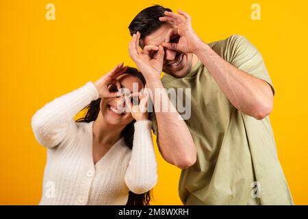 Sorridente marito e moglie arabo millenario fare gli occhiali con le mani, divertirsi insieme Foto Stock