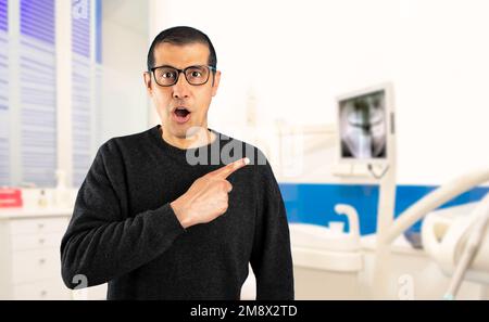 Uomo ispanico indossando maglione casual e occhiali a consulenza room.sorpresa puntando con il dito al lato, bocca aperta espressione stupita Foto Stock