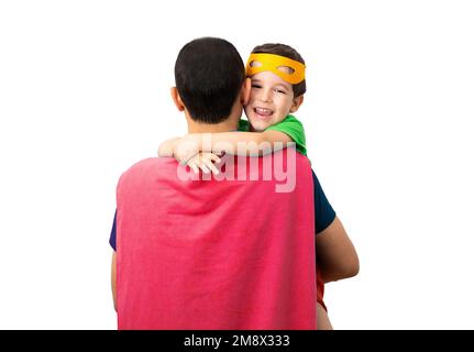Il ragazzino affettuoso abbraccia il padre con amore, indossa una maschera arancione, si veste in costume da supereroe, giocano insieme, isolati su un bac bianco Foto Stock