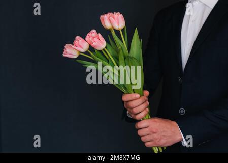 bouquet di tulipani rosa nelle mani degli uomini in tuta. Modello di biglietto d'auguri per le donne Foto Stock