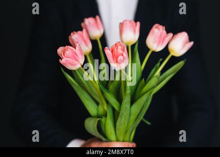 mazzo di tulipani rosa in mano maschile in tuta blu per un regalo per le vacanze primaverili Foto Stock