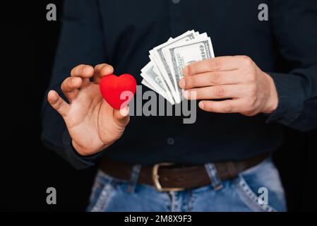 dollari e un cuore rosso nelle mani di un uomo. Il concetto di amore del denaro Foto Stock