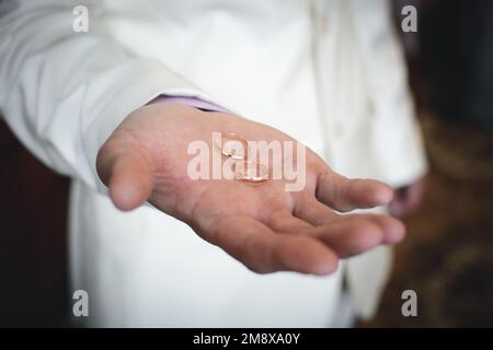 due anelli dorati per matrimoni si trovano sulla mano dell'uomo dello sposo in un vestito bianco Foto Stock