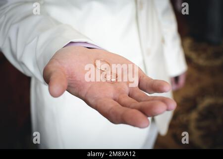 due anelli dorati per matrimoni si trovano sulla mano dell'uomo dello sposo in un vestito bianco Foto Stock