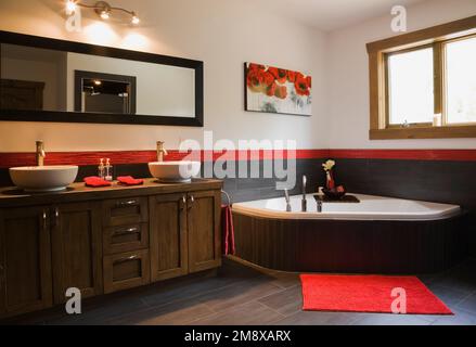 Bagno principale con armadietto in legno marrone con lavandini ciotola bianco e vasca incassata al piano superiore all'interno di una casa in legno di stile scandinavo. Foto Stock