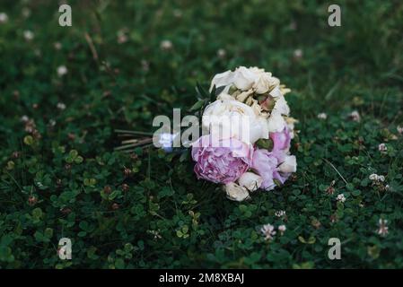 bel bouquet di nozze con rose bianche e peonie rosa adagiate sull'erba Foto Stock