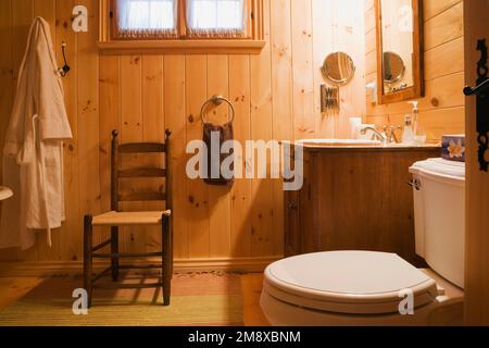 Antica sedia in legno con schienale alto, lavandino e WC nel bagno principale al piano superiore all'interno di una casa in legno macinato. Foto Stock