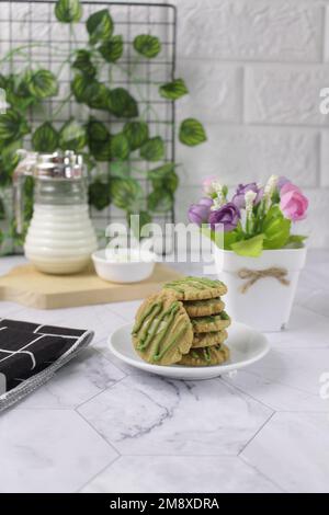 Biscotti al tè verde serviti su un piatto bianco con un bicchiere di latte sullo sfondo. Hanno un sapore leggermente dolce e una consistenza croccante. Foto Stock