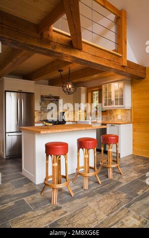 Isola di legno bianco con piano in legno e pelle rossa e sgabelli in legno in cucina all'interno di una cabina di tronchi fresata. Foto Stock