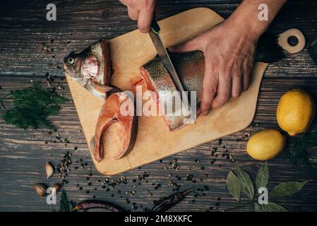 Lo chef maschile taglia pesce rosso fresco su un tavolo di legno in cucina Foto Stock