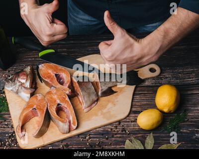 Pesce rosso fresco tagliato sul bordo e le mani del maschio chef. Trota cruda per cucinare Foto Stock