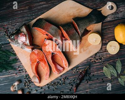 trota tagliata su un tavolo di legno con limone e condimenti. Pesce rosso fresco per cucinare Foto Stock