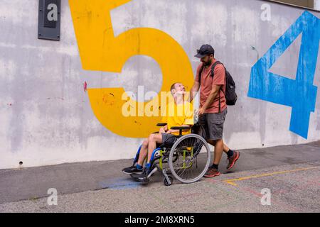 Disabile su sedia a rotelle con parete in cemento, divertendosi con un amico Foto Stock