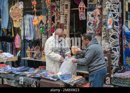 Street scene, negozio di tessuti, tappeti, uomini, pane, Bazar Khan el-Khalili, Città Vecchia, il Cairo, Egitto Foto Stock