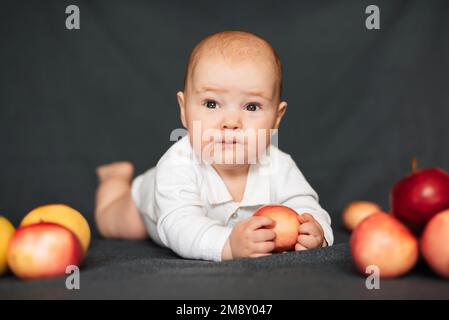 Neonato sdraiato con le mele. Bambino caucasico in un bodysuit bianco. Concetto di infanzia autunnale Foto Stock