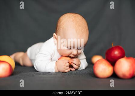 Neonato sdraiato con le mele. Bambino caucasico in un bodysuit bianco. Concetto di infanzia autunnale Foto Stock