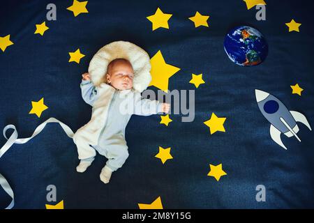 bambino piccolo che dorme in un vestito dell'astronauta sullo sfondo del cielo stellato con stelle e una nave spaziale. Vista dall'alto, giacitura piatta Foto Stock