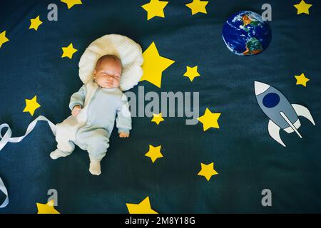 bambino piccolo che dorme in un vestito dell'astronauta sullo sfondo del cielo stellato con stelle e una nave spaziale. Vista dall'alto, giacitura piatta Foto Stock