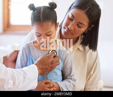 Ragazza piccola triste all'ufficio dei medici. Ragazza malata seduta con la madre mentre pediatra maschile ascoltare il battito cardiaco del petto. Medico di sesso maschile che esamina il bambino con Foto Stock