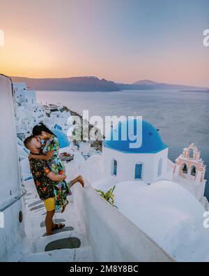 Santorini Grecia, giovane coppia di mezza età europea e asiatica in vacanza al villaggio greco di Oia Santorini Grecia, vacanza di lusso Santorini. Uomo e donna di mezza età guardando tramonto Santorini Foto Stock