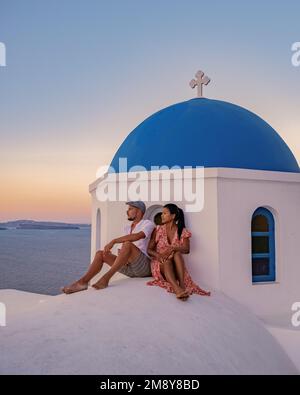 Santorini Grecia, giovane coppia di mezza età europea e asiatica in vacanza al villaggio greco di Oia Santorini Grecia, vacanza di lusso Santorini. Uomo e donna di mezza età guardando tramonto Santorini Foto Stock