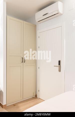 Chiusura di una porta frontale in legno bianco ad una stanza accanto ad un armadio. Le porte del guardaroba sono dipinte di beige e chiuse da occhi indiscreti. Aria condizionata Foto Stock