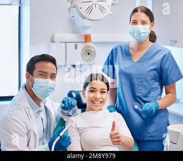 Dandole il permesso di sorridere. un giovane dentista maschio che dà i pollici in su con il suo paziente ed assistente. Foto Stock
