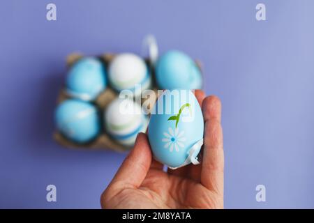 womans mano che tiene pasqua colorate uova dipinte a mano blu in una scatola su peri fondo molto. Foto Stock
