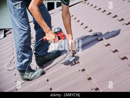 Lavoratore prepearing per l'installazione di pannelli solari fotovoltaici sul tetto della casa. Primo piano man installer che lavora con il cacciavite elettrico. Foto Stock