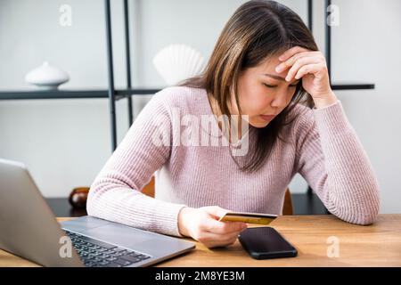 Stressato femmina hold carta di credito calcolare il reddito mensile delle spese domestiche è soldi non abbastanza con il laptop Foto Stock