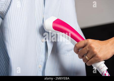 Primo piano della donna che utilizza il generatore di vapore elettrico a mano esce vapore per vestiti camicia Foto Stock